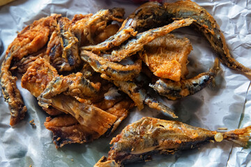 Deep fried sardine lies on oiled paper.