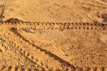 Trace of a car wheel on on the mud, soil land. Driving on desert sand after rain. Car tread pattern. Texture of a road with traces of car tires. Track, tracks. Footprint, Footprints
