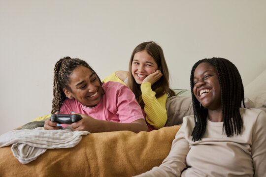 Cheerful teenage girl holding game controller while enjoying with female friends at home