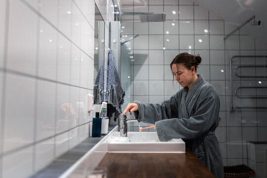 Side view of young woman washing toothbrush in sink at bathroom