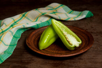 Clay plate with whole and halves of green bell pepper and green kitchen towel on wooden background....