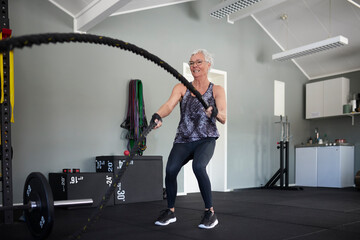 Full length of active senior woman exercising with ropes at health club
