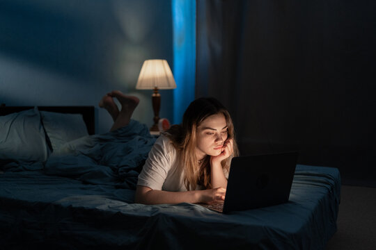 Young woman relaxing in bed with laptop computer at night