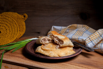 Clay plate of fried meat pies with cutlery and green onion on wooden table.