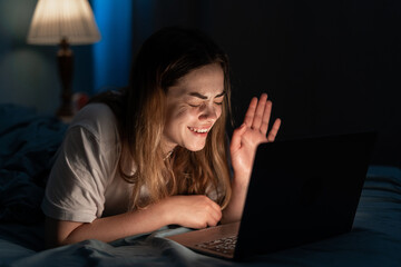 Young woman resting in bed at night watching movie laughing enjoying comedy late at night