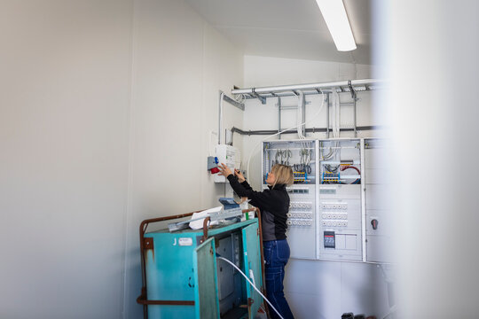 Female electrician installing fuse box while standing in meter room at industry