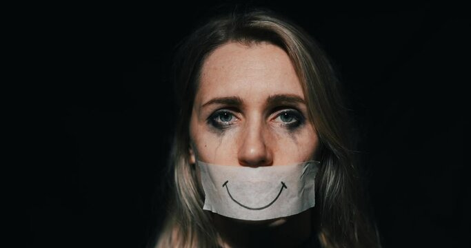 abuse and domestic violence. sad depressed woman hide her mouth behind fake drawn smile on paper tape. depression and mental health