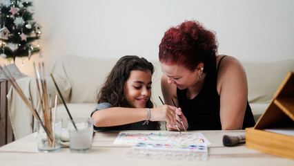 Latin mother and child son painting with watercolors during Christmas time at home. Holiday, Love...