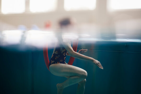 Side view of woman exercising with noodle float in swimming pool