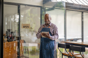 A healthy retired black senior man stands proudly at his new personal business. Hold a tablet to...