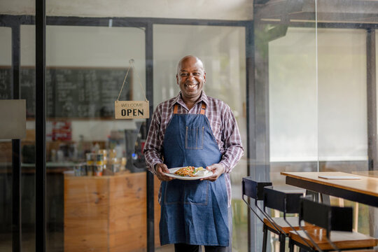 A healthy retired black senior man stands proudly at his new personal business. Show his recommended menu. Startup business owner. SME entrepreneurs.