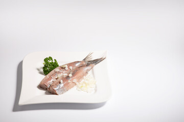 Raw salted dutch new herring with sliced union parts on a white plate on a white background