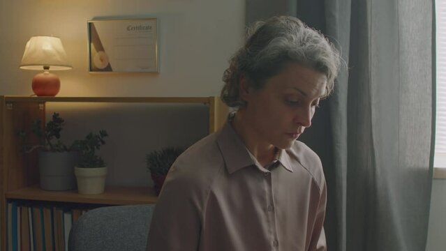 Zoom in shot of mature female doctor sitting in clinic and using laptop while examining health of patient