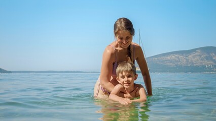 Fototapeta na wymiar Little boy learning swimming in the sea with happy mother. Family holiday, vacation and fun summertime of children and parents.