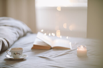 Light cozy bedroom, Coffee or tea cup and an open book on the bed. Spring still life. Breakfast in...