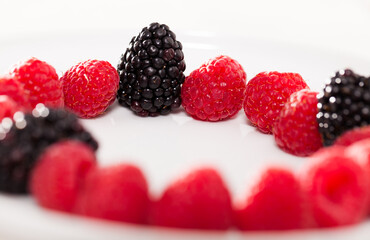 Raspberries and blackberries laid out on a white plate in circle
