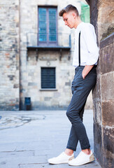 Young European guy in shirt and trousers with suspenders walking around city