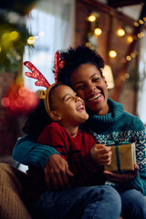 Cheerful black mother and daughter on Christmas day at home. - obrazy, fototapety, plakaty