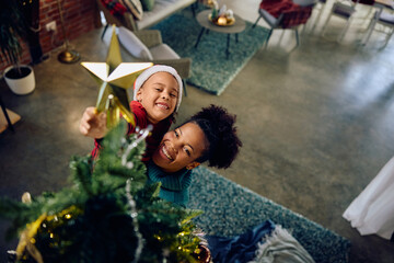 Happy black mother with daughter decorating Christmas tree at home.