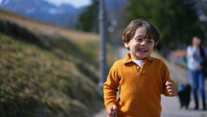 Joyful excited little boy running outside during autumn day wearing yellow pullover. Close-up face of child in motion sprinting forward feeling carefree