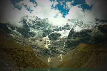 Snow capped mountain overlooking a glacial lake in The Peruvian Andes - obrazy, fototapety, plakaty