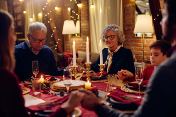 Extended family praying during Christmas dinner at dining table.