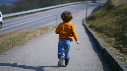 From behind, a spirited child in a yellow pullover, jeans, and boots sprints with delight through...