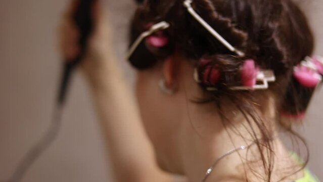 Selective focus on woman blowing dry her dark hair with curlers, self-care routine with styling hair