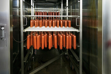 Fresh smoked sausage suspended on a rope on a metal frame in the smokehouse of meat plant.