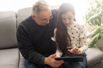 Senior man with his grandchild looking together on photos in tablet