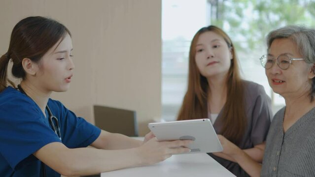 In the clinic at the Reception Desk, Asian nurse talking with a mother and her daughter at counter in hospital. She is typing on her tablet, Mother and daughter made a doctor's appointment.