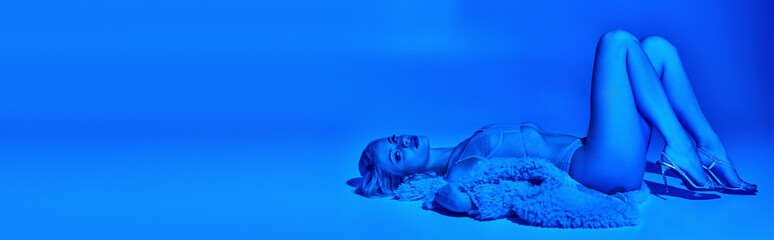 appealing woman in erotic lingerie and faux fur lying on floor surrounded by blue lights, banner
