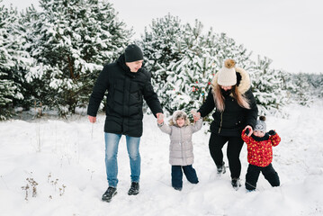 Happy family walking near decorated Christmas tree having fun in winter forest. Winter holidays, new year concept. Mom, dad, son, daughter playing in snow. Father, mother, children enjoying trip.