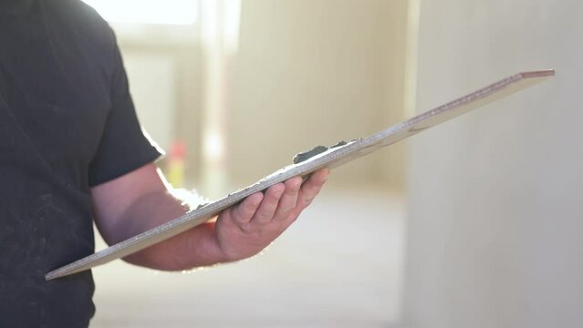 Professional tiler applying adhesive glue to tile for tiling the floor, industry building concept