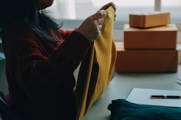 Startup SME small business entrepreneur of freelance Asian woman wearing apron using laptop and box to receive and review orders online to prepare to pack sell to customers, online sme business ideas.