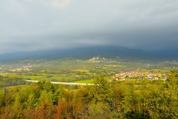 View of Vipava valley lit by sunlight and hills above covered in clouds and Cesta village in Primorska, Slovenia