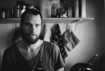 Home, man and portrait in a kitchen with drink and monochrome with black and white. Male person, calm smile and beard ready for cooking in a house with a beverage and drink relax with alcohol and art