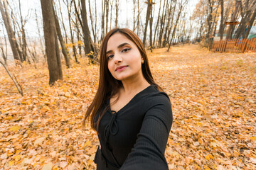Close-up portrait of diversity young beautiful confident Indian Asian woman in black dress in fall outdoor copy space mockup. Happy and natural smiling female. Generation z and gen z youth concept