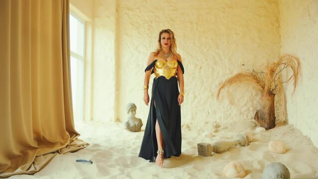fantasy sexy woman walking in room full sand desert. blonde hair beauty face. fashion model girl in black long dress golden corset warrior armor gold old style. barefoot steps art creative video 4k