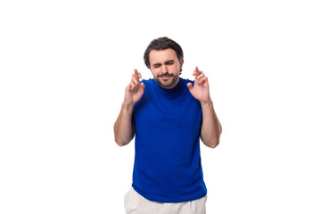 Fototapeta premium young brunette man with a beard dressed in a blue t-shirt crossed his fingers in hope on a white background