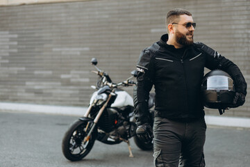 Man biker standing by his motorbike holding his helmet