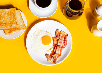 Fried egg with roasted bacon, black coffee, toasts on yellow background. Retro American breakfast....