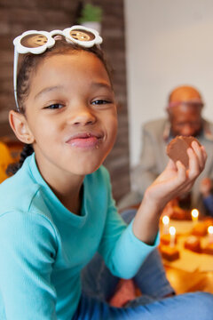 Little biracial girl wearing sunglasses on head eating cake celebrating birthday