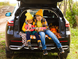 Little cute smiling girl and boy sitting in open car trunk. Kid resting with her family in the nature. Autumn season.