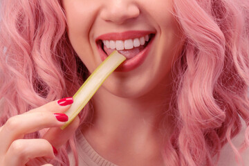 Celery sticks in a woman hand. Woman with pink curly hair is eating celery.