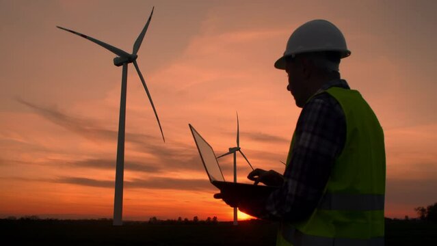 Young Man maintenance engineer works at a wind farm at sunset with