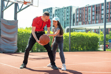 Happy father and teenage daughter playing basketball outside at court