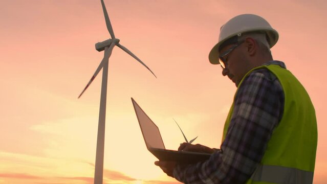 Engineer protective helmet at windmills checks operation turbines using a laptop