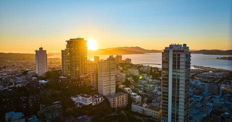 Fototapeta premium Aerial sun behind mountain seen through San Francisco skyscraper buildings at sunset, CA