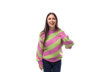 Obraz na płótnie Canvas young caucasian woman with black hair dressed in a pink striped sweater points with her hand on a white background with space for advertising